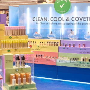 A Sephora store display featuring various CLEAN makeup products arranged by category, such as tinted coverage, lips, sculpting, and more. The backdrop reads CLEAN, COOL & COVETED in a bright, colorful setting.