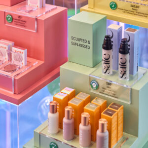 A vibrant retail display showcases skincare and makeup products in various shades. Boxes and bottles proudly feature the Sephora Clean label, with prices starting from $27. The items are neatly organized on pastel stands, embodying both style and safety.
