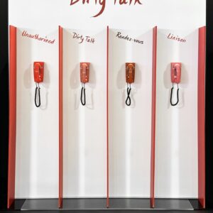 A NARS Custom Display for Dirty Talk showcases four red retro telephones. Each is placed in its own section, labeled Unauthorized, Dirty Talk, Rendez-vous, and Liaison. This intriguing wall display invites you to explore each connection with a touch of bold nostalgia.
